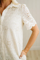 Blonde woman wearing a button front collared shift dress with scalloped edges, and all over eyelet lace embroidery in cream.