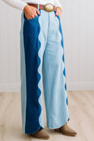 BLONDE WOMAN IN A BRIGHTLY LIT STUDIO WEARING A WHITE SWEATER, BROWN BELT AND SCALLOP WAVE DENIM OCEAN CURVE JEANS WITH TWO TONES.
