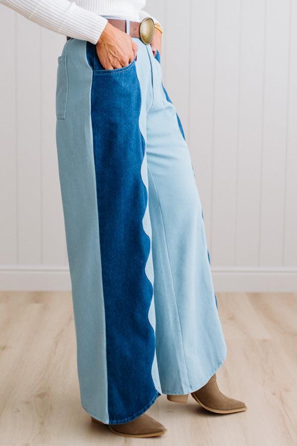 BLONDE WOMAN IN A BRIGHTLY LIT STUDIO WEARING A WHITE SWEATER, BROWN BELT AND SCALLOP WAVE DENIM OCEAN CURVE JEANS WITH TWO TONES.