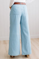 BLONDE WOMAN IN A BRIGHTLY LIT STUDIO WEARING A WHITE SWEATER, BROWN BELT AND SCALLOP WAVE DENIM OCEAN CURVE JEANS WITH TWO TONES.