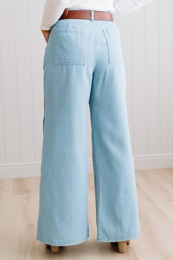 BLONDE WOMAN IN A BRIGHTLY LIT STUDIO WEARING A WHITE SWEATER, BROWN BELT AND SCALLOP WAVE DENIM OCEAN CURVE JEANS WITH TWO TONES.