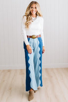 BLONDE WOMAN IN A BRIGHTLY LIT STUDIO WEARING A WHITE SWEATER, BROWN BELT AND SCALLOP WAVE DENIM OCEAN CURVE JEANS WITH TWO TONES.