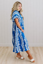 Woman wearing a blue and white patterned dress standing against a white paneled wall.