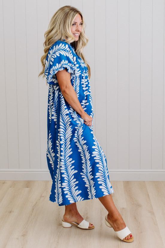 Woman wearing a blue and white patterned dress standing against a white paneled wall.
