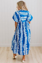 Woman wearing a blue and white leaf pattern dress against a white wall.