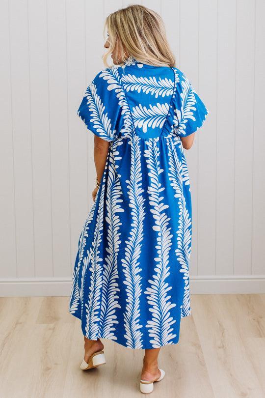 Woman wearing a blue and white leaf pattern dress against a white wall.