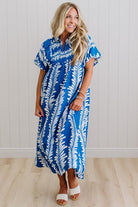 Woman wearing a blue and white patterned dress against a white wall.