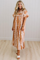 Woman wearing a brown and white patterned dress against a white wall.