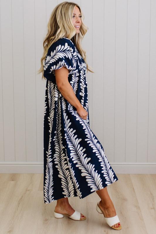 Woman wearing a navy and white patterned dress standing against a white paneled wall.