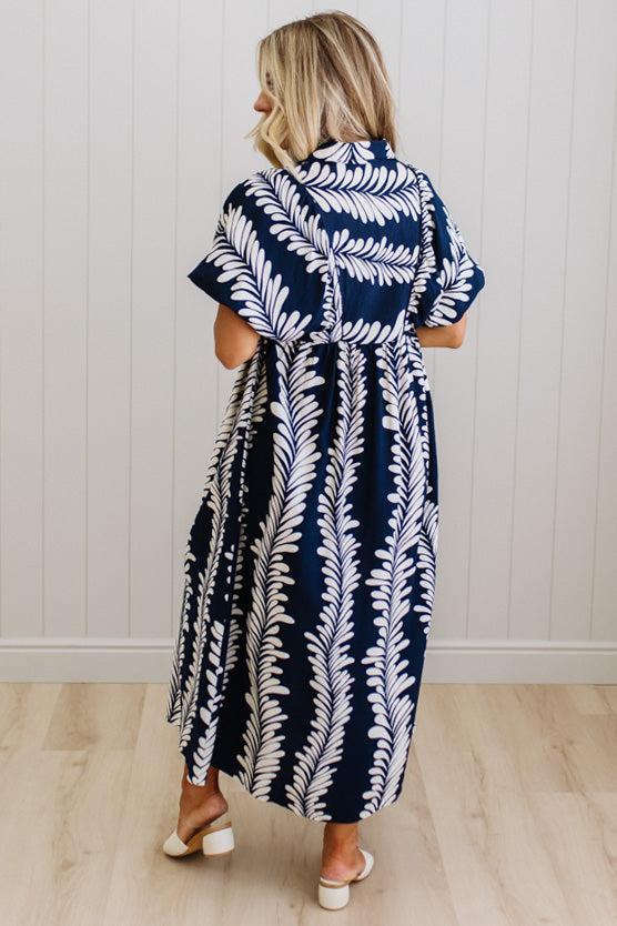 Woman wearing a navy and white patterned dress against a white wall.