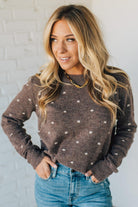 Woman wearing a brown polka dot sweater against a white brick wall