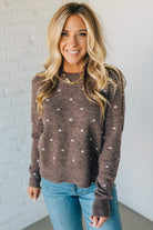 Woman wearing a brown polka dot sweater and blue jeans against a white brick wall.