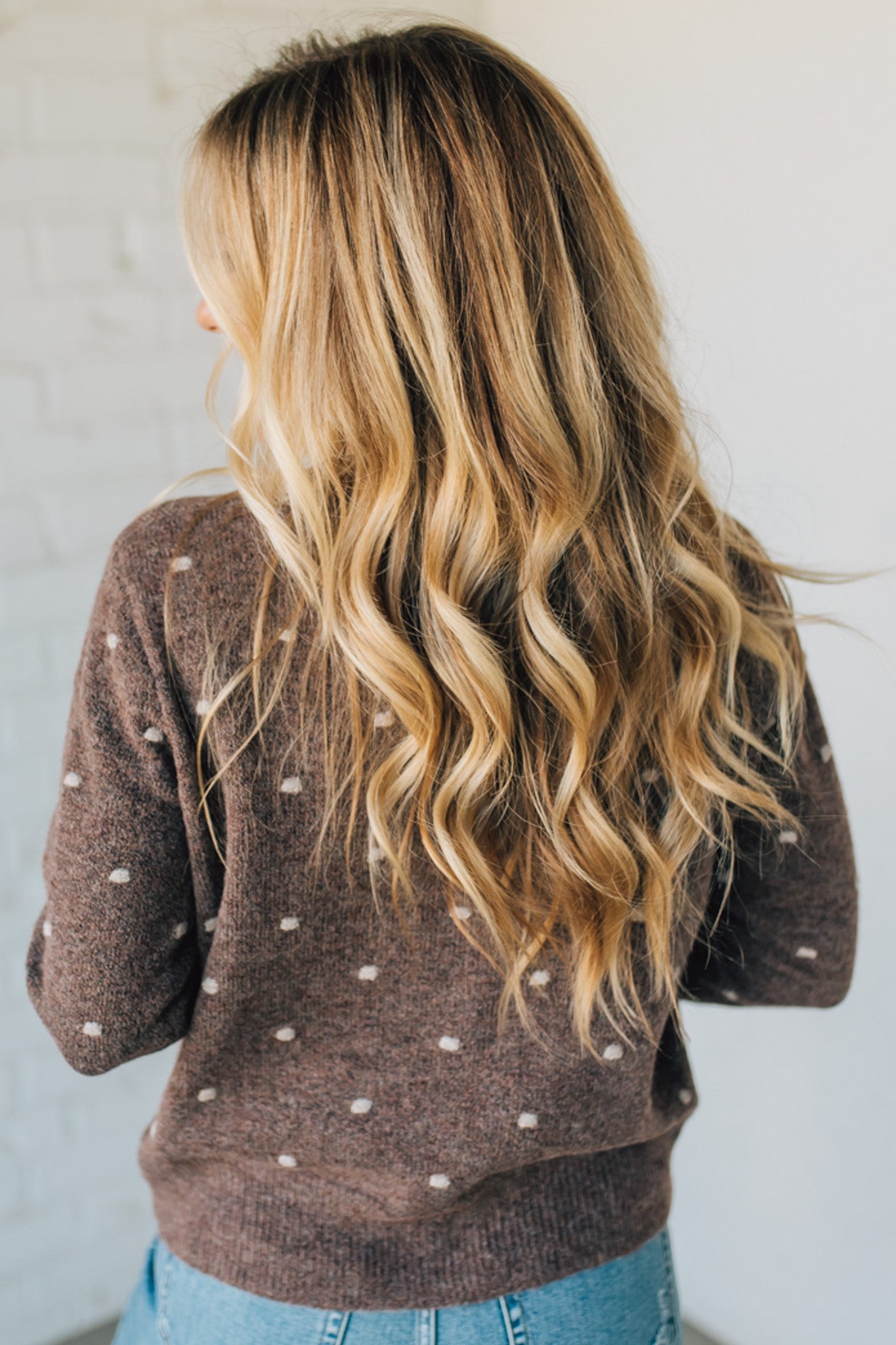 Person wearing a brown polka dot sweater with long blonde hair against a plain background