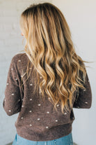Person wearing a brown polka dot sweater with long blonde hair against a plain background