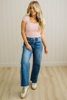 Woman wearing a striped top and blue jeans standing in a room with a light wooden floor and white paneled walls.