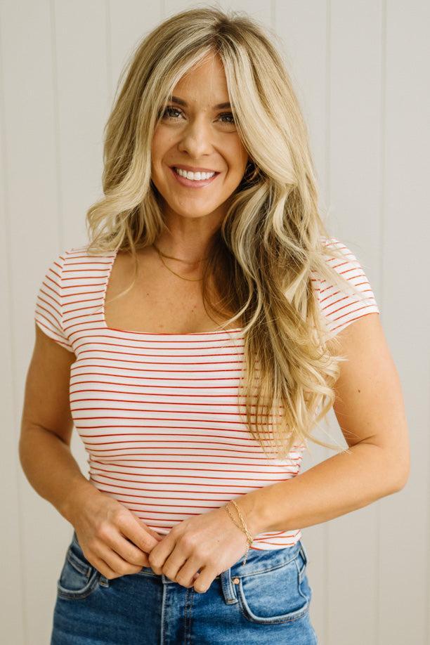 Woman wearing a red and white striped shirt and blue jeans against a plain background
