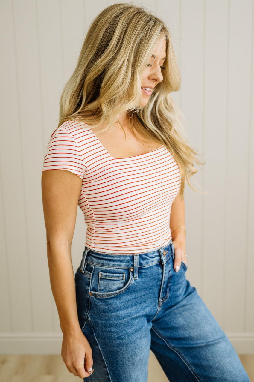 Woman wearing a red and white striped shirt and blue jeans against a neutral background