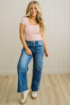 Woman wearing a striped shirt and blue jeans standing against a plain wall.
