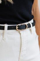 Close-up of a person wearing a black shirt, jeans, and a black belt with a gold buckle.