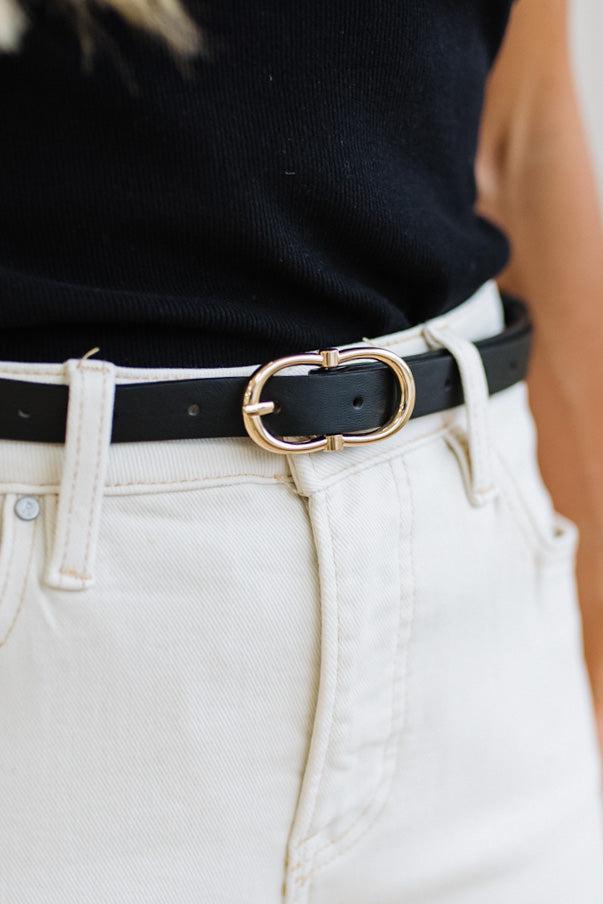 Close-up of a person wearing a black shirt, jeans, and a black belt with a gold buckle.