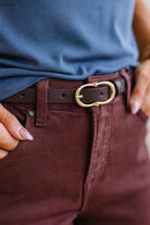 Close-up of a person wearing a blue shirt, jeans, and a brown belt with a gold buckle.