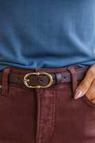 Close-up of a person wearing a blue shirt, jeans, and a brown belt with a gold buckle.