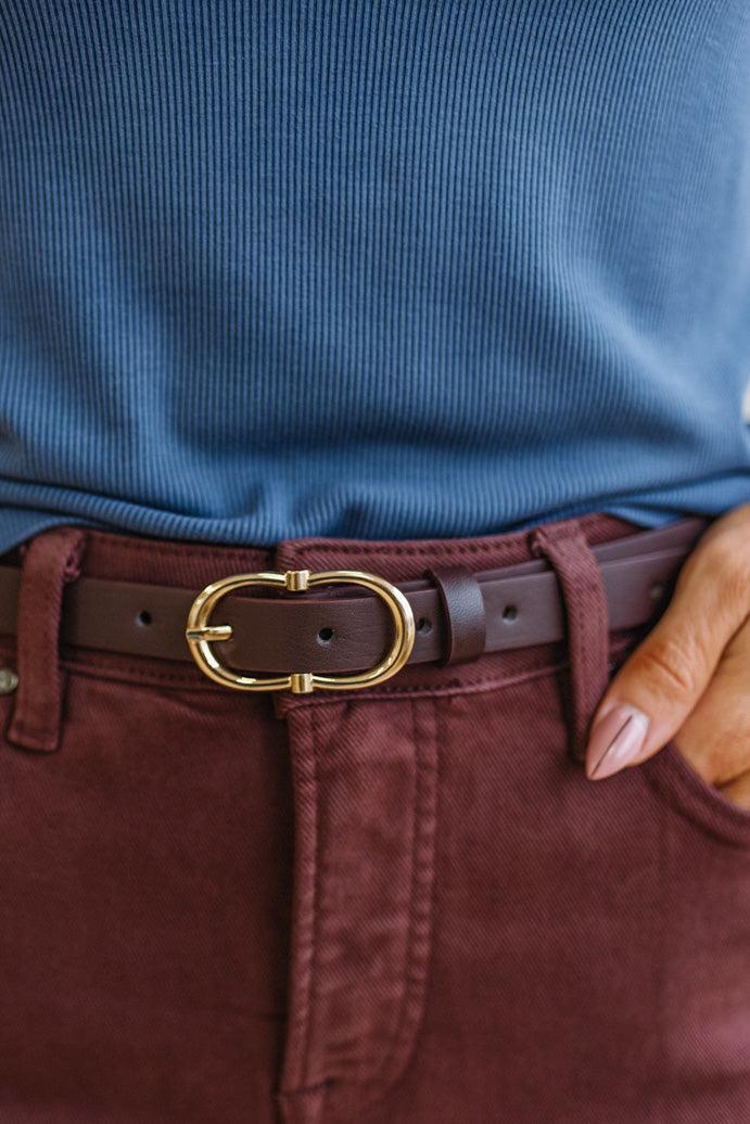 Close-up of a person wearing a blue shirt, jeans, and a brown belt with a gold buckle.