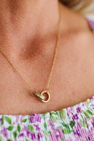 Gold necklace with a small pendant on a person wearing a floral top.