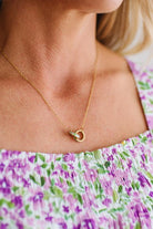 Close-up of a person wearing a gold necklace with a heart pendant, against a floral-patterned garment.