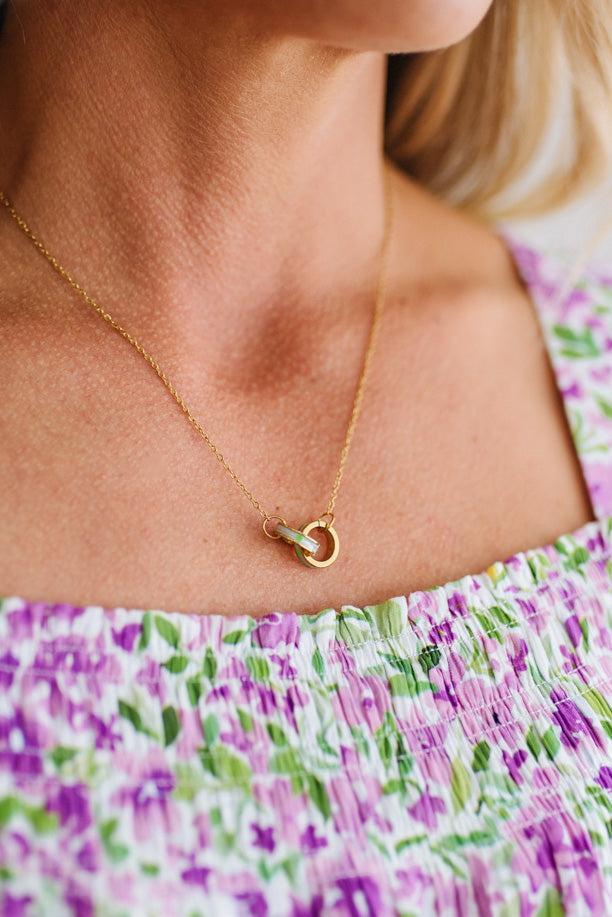 Close-up of a person wearing a gold necklace with a heart pendant, against a floral-patterned garment.