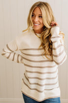 Woman wearing a beige and brown striped sweater against a white wall.