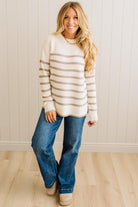 Woman wearing a striped sweater and jeans standing against a white paneled wall.