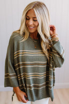 Blonde woman wearing an olive green sweater with neutral stripes and 3/4 length sleeves,  with a loose fit.