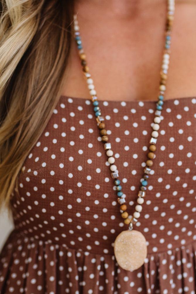 Long beaded necklace with a pendant worn by a person in a brown polka dot dress.