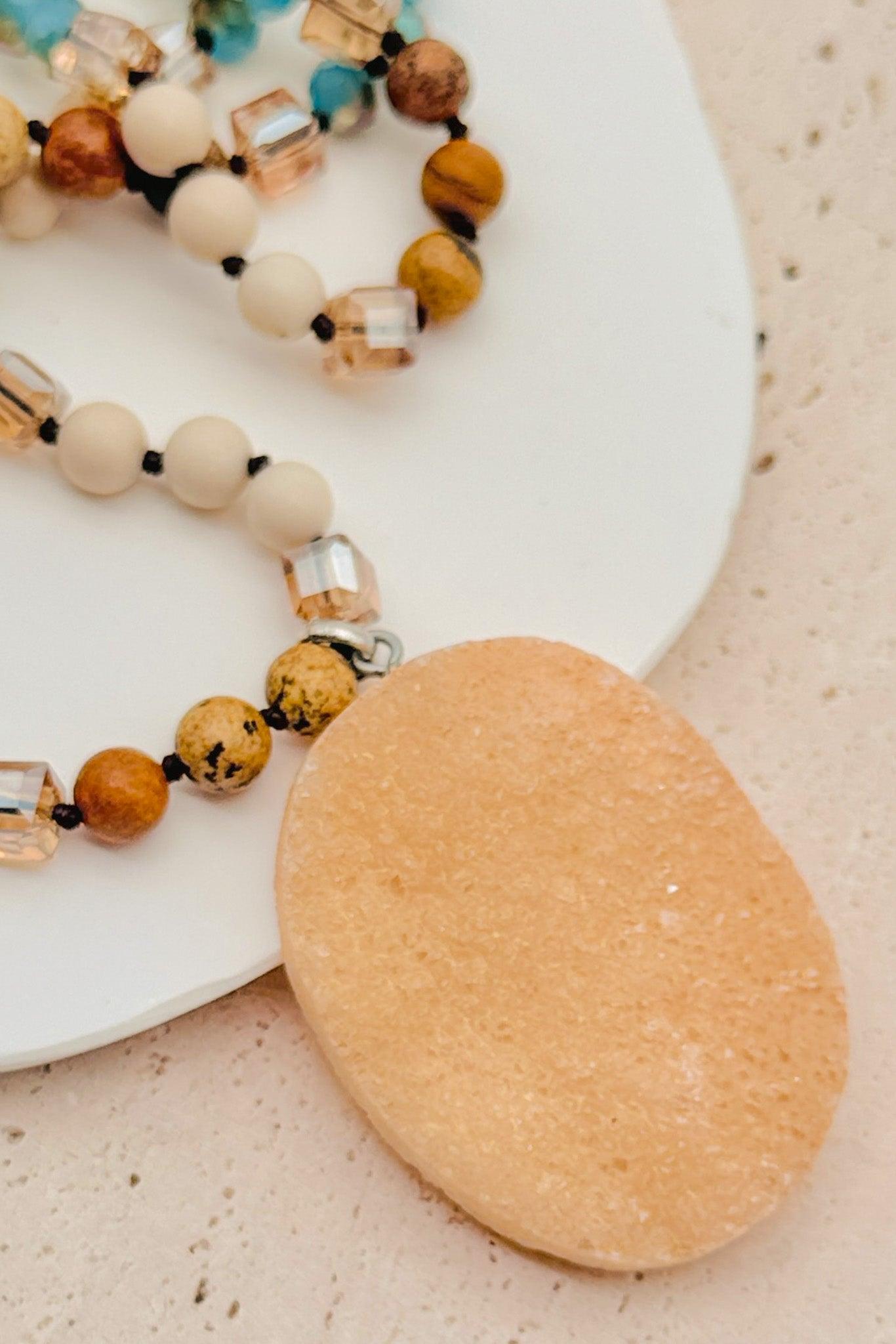 Necklace with beads and a large beige stone on a light surface