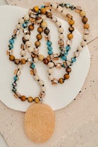 Beaded necklaces with a large beige pendant on a textured surface
