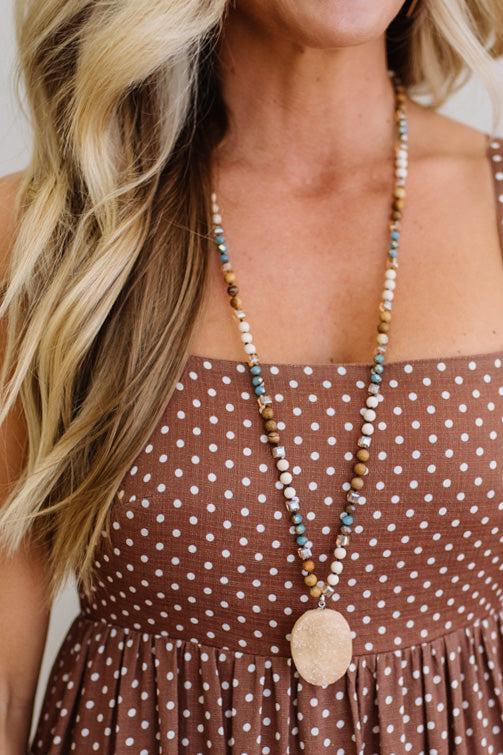 Woman wearing a long beaded necklace with a brown polka dot dress.