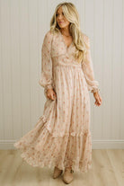 Woman wearing a long, flowing dress with a floral pattern against a white paneled wall.