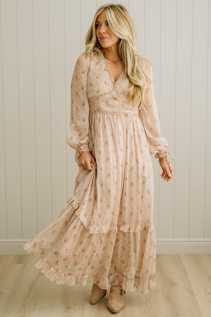 Woman wearing a long, flowing dress with a floral pattern against a white paneled wall.