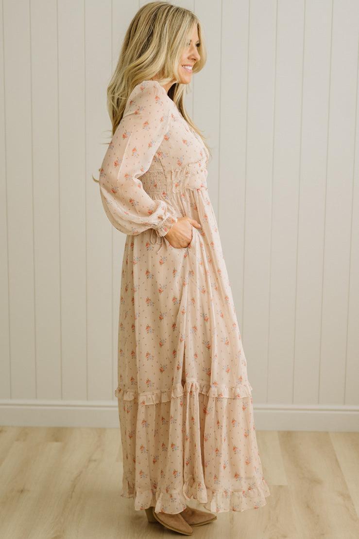 Woman wearing a long, light-colored dress with a subtle pattern against a white paneled wall.