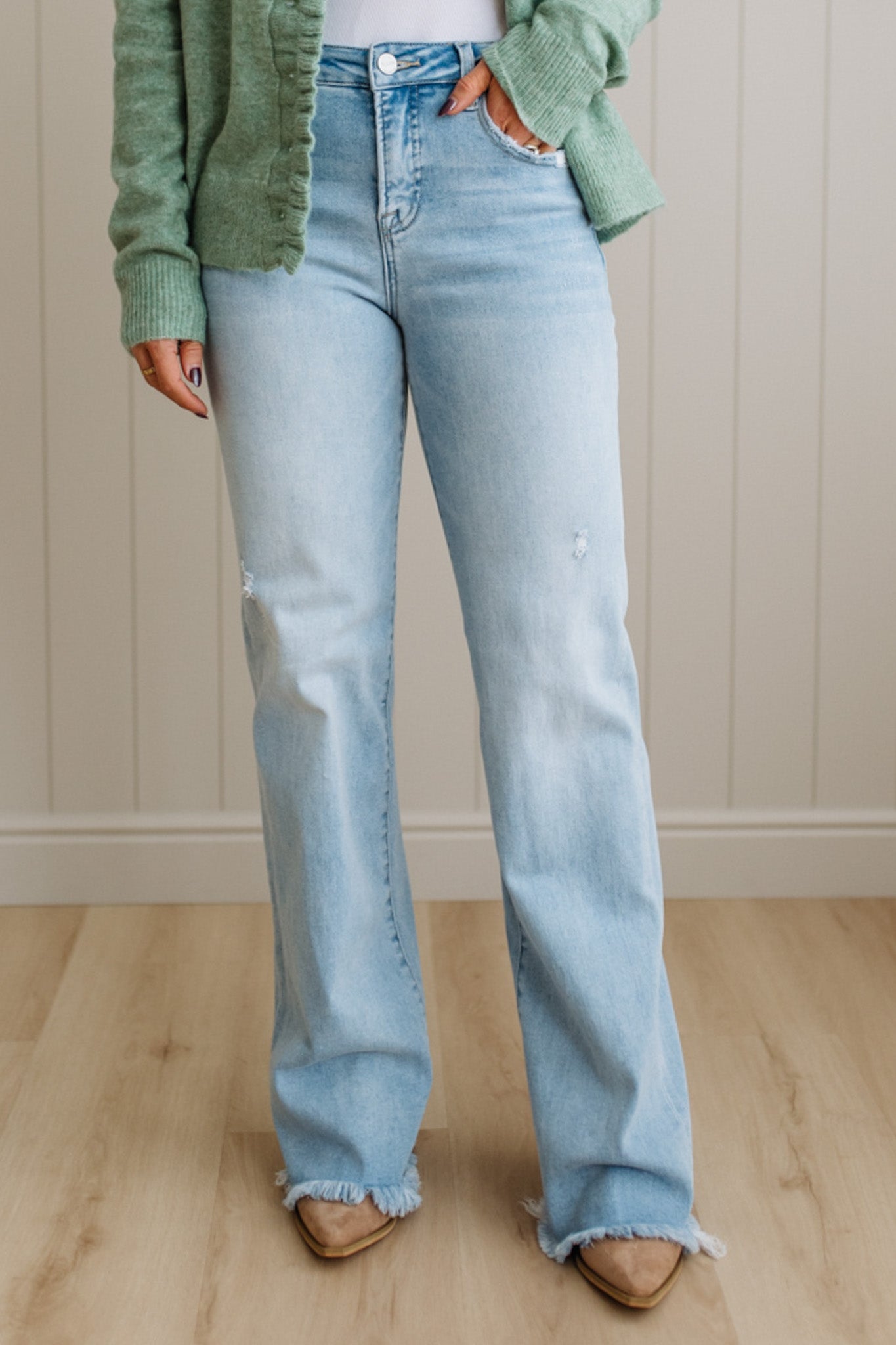 Person wearing light blue jeans and a green cardigan against a neutral background