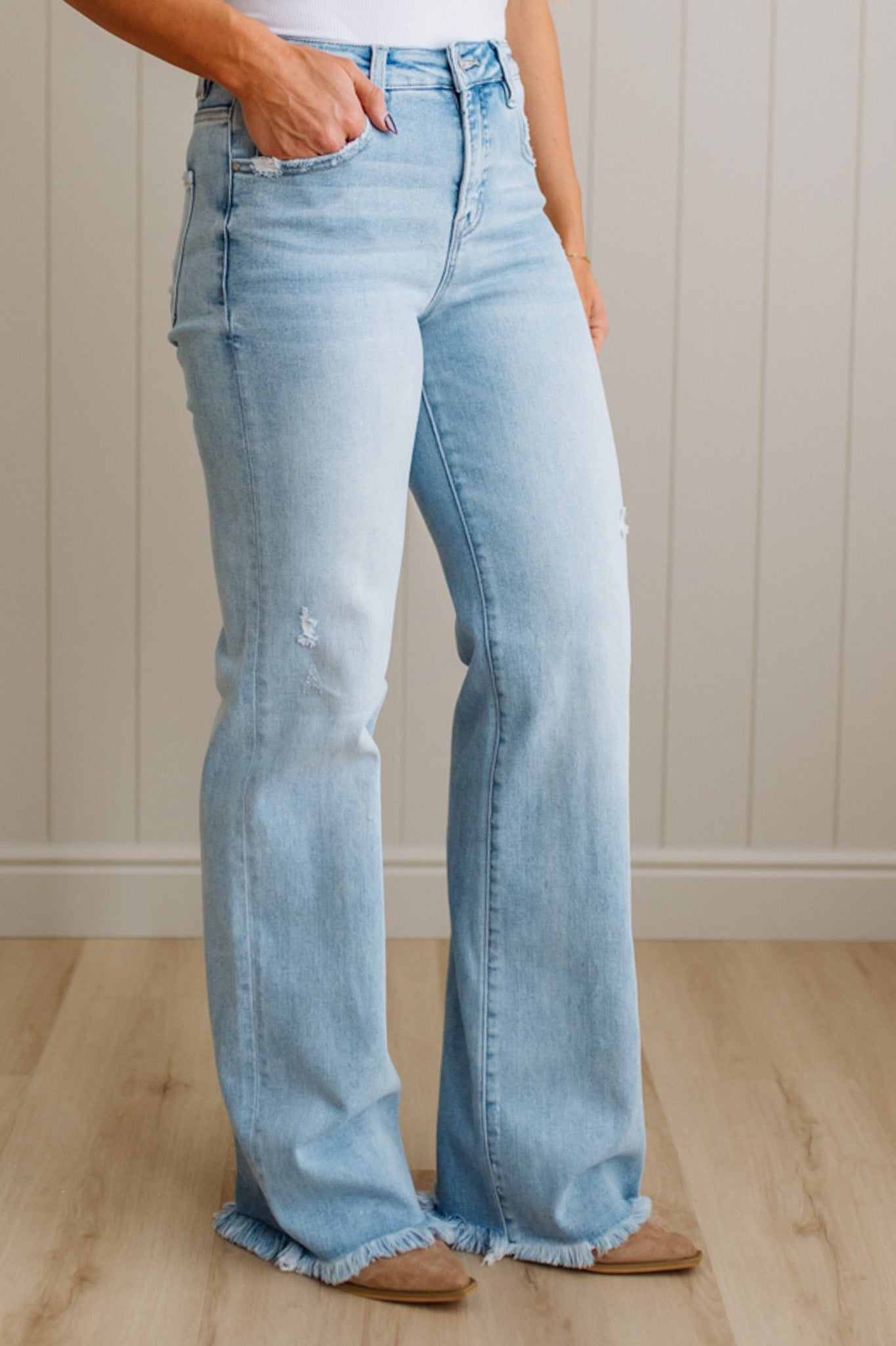 Light blue flared jeans worn by a person on a wooden floor with a white paneled wall background.