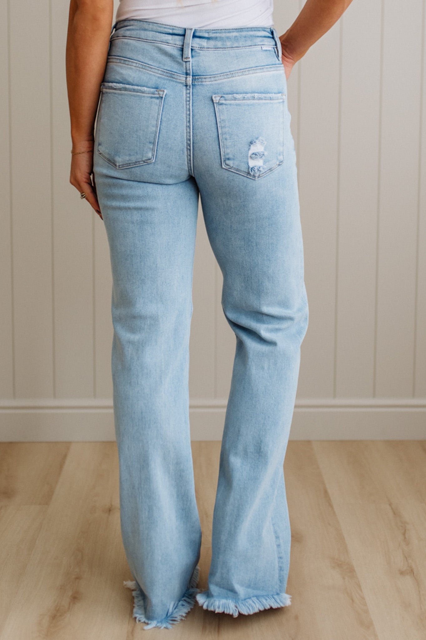 Light blue jeans worn by a person on a wooden floor with a neutral wall background