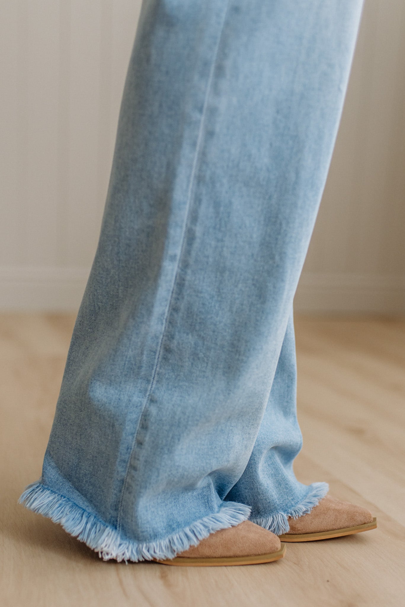 Light blue jeans with frayed hem worn by a person on a wooden floor.