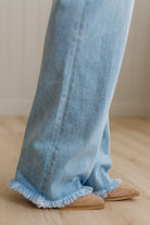 Light blue jeans with frayed hem worn by a person on a wooden floor.