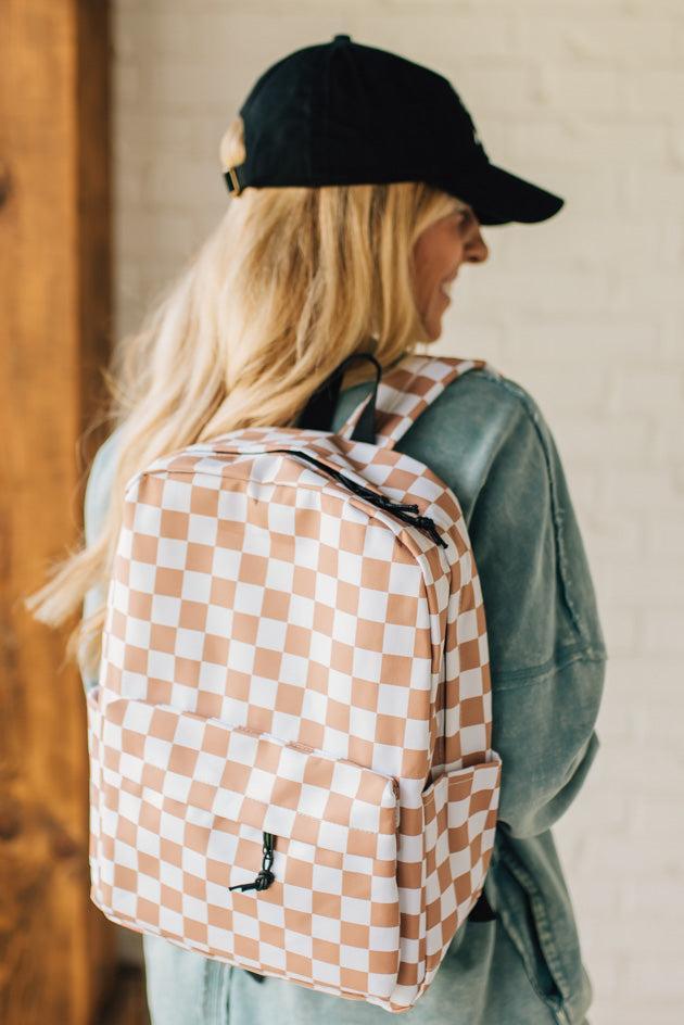 Blonde woman in a black hat with a mocha and and white checkered backpack with black zipper and tag pulls.