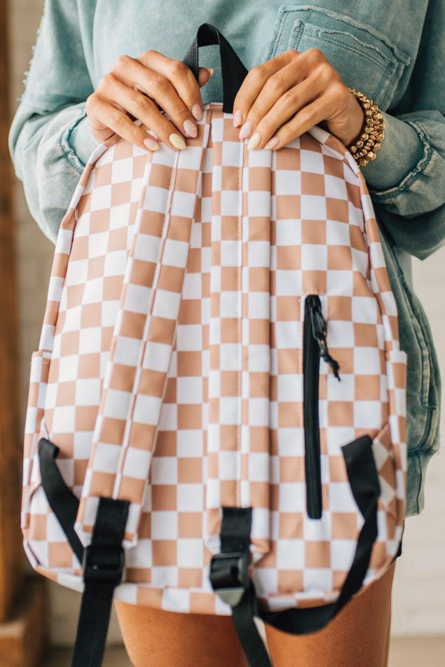 Blonde woman in a black hat with a mocha and and white checkered backpack with black zipper and tag pulls.