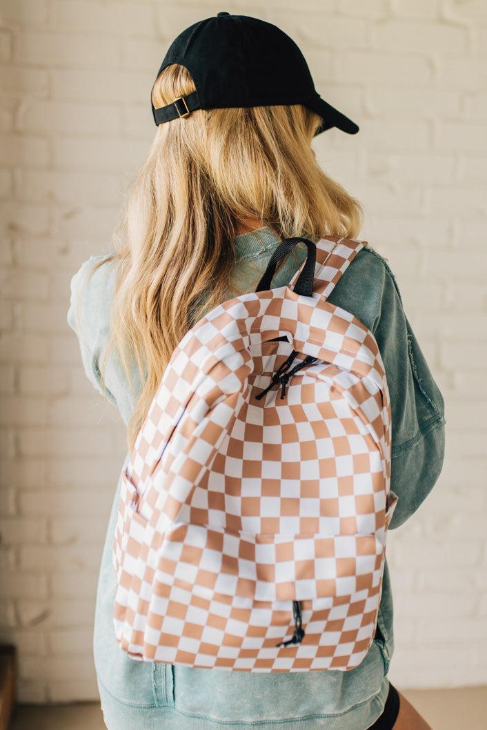 Blonde woman in a black hat with a mocha and and white checkered backpack with black zipper and tag pulls.