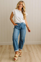 Woman wearing a white top with lace sleeves and blue jeans against a light wooden paneled wall.