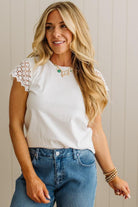 Woman wearing a white lace-trimmed top and blue jeans against a neutral background